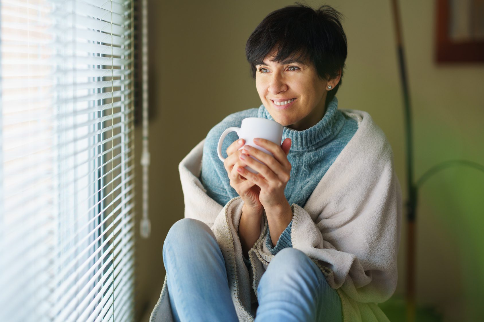 Woman in her forties with a cup of coffee by a window, reflecting on her hormone health